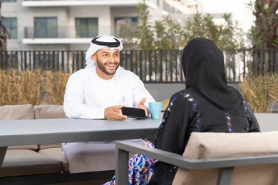 Arab man showing his wife a souvenir photo, gestures of pleasure and happiness, honeymoon, enjoying hot drinks, concept of affection and intimacy, spending a pleasant time, smiling Arab Gulf Emirati couple sitting in a cafe