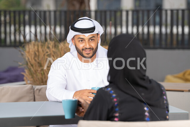 ايماءات السرور والسعادة ، قضاء أوقات ممتعة ورومانسية، الاستمتاع بشرب المشروبات الساخنه ، مفهوم المودة والالفة ، زوجان عربيان خليجيان اماراتيان مبتسمان يجلسان في المقهى