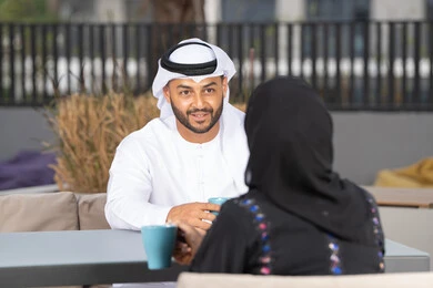 Gestures of pleasure and happiness, spending enjoyable and romantic times, enjoying hot drinks, the concept of affection and intimacy, a smiling Emirati Gulf Arab couple sitting in a café