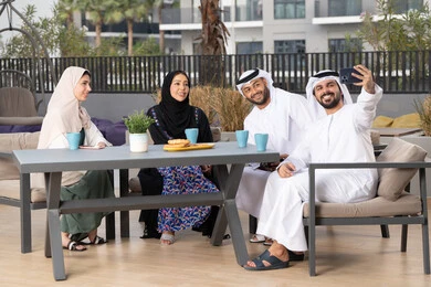 Emirati man taking selfies with his mobile phone, family entertainment activities and events, happy family atmosphere full of love, the concept of intimacy and love between family members, gestures of pleasure and happiness, entertainment and recreation during holidays, enjoying drinking hot drinks, an Arab Gulf Emirati family sitting in a cafe