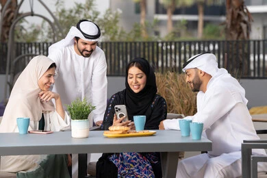 الاستمتاع بشرب المشروبات الساخنه ، عائله عربيه خليجيه اماراتيه تجلس في المقهى ، سيدة اماراتية تستخدم الجوال ، أجواء اسرية سعيدة مليئة بالحب، مفهوم الألفة والمحبة بين أفراد الأسرة، انشطة وفعاليات ترفيهية عائلية، ايماءات السرور والسعادة، التسلية والترفيه بالعطلات