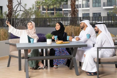 أجواء اسرية سعيدة مليئة بالحب، مفهوم الألفة والمحبة بين أفراد الأسرة، سيدة اماراتية تلتقط صور السيلفي التذكارية عبر الجوال ،انشطة وفعاليات ترفيهية عائلية، ايماءات السرور والسعادة، التسلية والترفيه بالعطلات ، الاستمتاع بشرب المشروبات الساخنه ، عائله عربيه خليجيه اماراتيه تجلس في المقهى