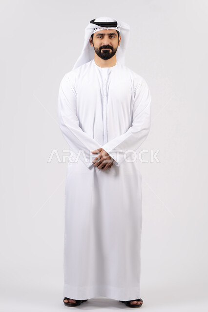 الوقوف باستقامة وثقة بالنفس،الأناقة والاهتمام بالمظهر الخارجي، مفهوم الرجولة والقوة،بورتريه لرجل عربي خليجي إماراتي يرتدي الكندورة الاماراتية والغترة ينظر إلى الكاميرا ، الطول الكامل للجسم، خلفية بيضاء