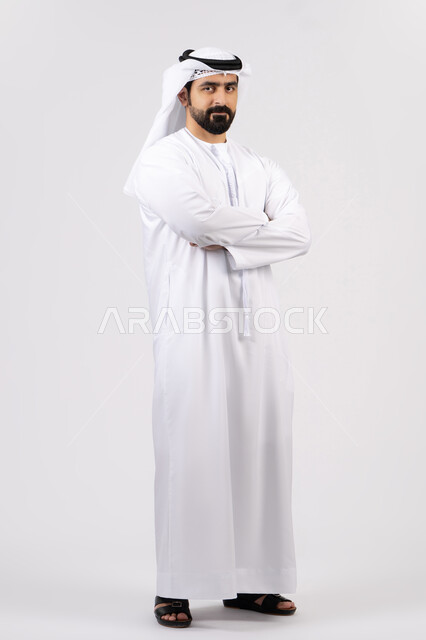 Elegance and interest in outward appearance, the concept of masculinity and strength, a portrait of an Emirati Gulf Arab man wearing the Emirati kandura and ghutra, looking at the camera, standing straight and confident, full body length, white background