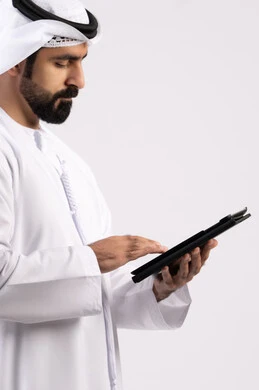 Gestures of concentration and integration, use of modern technology, portrait of an Emirati Gulf Arab man wearing a kandura and ghutra using a tablet, integration of modern technology into practical life, displaying a blank black screen, a full body image, a white background