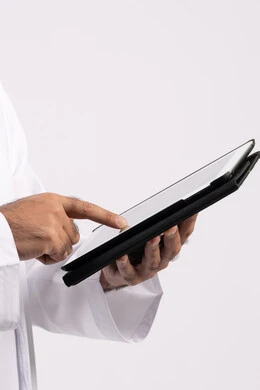 استخدام التكنولوجيا الحديثة ،بورتريه ليد رجل عربي خليجي اماراتية ترتدي الكندورة والغترة يقوم باستخدام الجهاز اللوحي ،ايماءات التفاعل والاندماج , دمج التقنيات الحديثة في الحياة العملية، عرض شاشة سوداء فارغة، صورة للجسم بالكامل، خلفية بيضاء