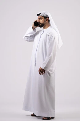 Integrating modern technology and technology into daily life, making phone calls, pointing at the mobile phone screen, chatting with family and friends, portrait of an Emirati Gulf Arab man wearing a kandura holding a mobile phone, white background.