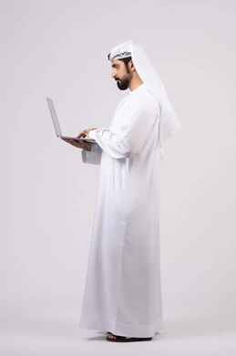 تصفح مواقع التواصل الإجتماعي ،ادارة شؤون الاعمال وتنظيمها، استخدام الأجهزة التقنية الحديثة والمتطورة، العمل عن بعد،  بورتريه لرجل عربي خليجي اماراتي يرتدي الكندورة والغترة البيضاء يستخدم الحاسوب المحمول، اجراء مكالمات الفيديو، خلفية بيضاء