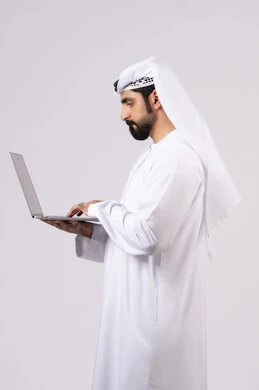 Working remotely, browsing social media, managing and organizing business affairs, using modern and advanced technical devices, portrait of an Emirati Gulf Arab man wearing a white kandura and ghutra using a laptop, making video calls, white background