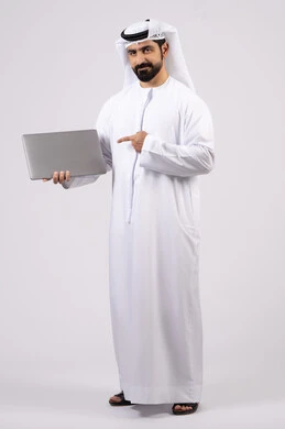 الاشارة الى جهاز اللابتوب، ادارة شؤون الاعمال وتنظيمها، العمل عن بعد، تصفح مواقع التواصل الإجتماعي ،استخدام الأجهزة التقنية الحديثة والمتطورة، بورتريه  لرجل عربي خليجي اماراتي يرتدي الكندورة والغترة البيضاء يستخدم الحاسوب المحمول، اجراء مكالمات الفيديو، خلفية بيضاء