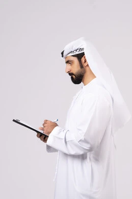 Portrait of a young Emirati Arab man wearing a kandura and ghutra holding a bunch of white papers and a pen, recording notes and information on paper, writing down daily tasks and goals, organizing and managing business, writing down daily tasks, white background