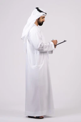 بورتريه لشاب عربي خليجي اماراتي يرتدي الكندورة والغترة يقوم بكتابة المهام والأهداف اليومية, تنظيم وإدارة الأعمال ، تدوين وتسجيل الملاحظات والمعلومات على الورق, خلفية بيضاء