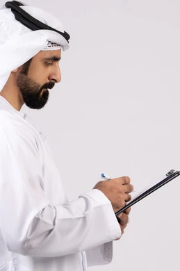 تدوين وتسجيل الملاحظات والمعلومات على الورق, بورتريه لشاب عربي خليجي اماراتي يرتدي الكندورة والغترة يقوم بكتابة المهام والأهداف اليومية, تنظيم وإدارة الأعمال ، خلفية بيضاء