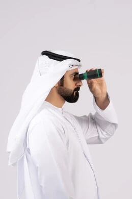 Portrait of an Emirati Gulf Arab man wearing a kandura and ghutra looking through binoculars. A love of adventure and exploration, seeing distant objects through a telescope, gestures and expressions of surprise and amazement, white background