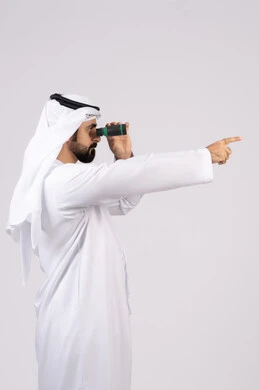 الاشارة الى شئ بعيد، بورتريه لرجل عربي خليجي إماراتي مبتسم يرتدي الكندورة والغترة ينظر من خلال المنظار ثنائي العينين، حب المغامرة والاستكشاف، رؤية الاشياء البعيدة عبر التلسكوب،ايماءات وتعابير الدهشة والمفاجئة، خلفية بيضاء