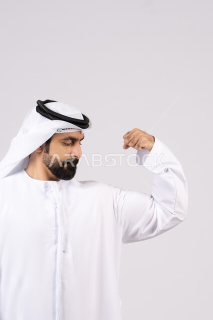 Portrait of an Emirati Gulf Arab man showing muscles, making hand gestures indicating strength and courage, healthy physique, fitness concept, having a healthy body, white background