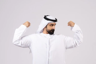 بورتريه لرجل عربي اماراتي خليجي يقوم بعرض العضلات، التمتع بجسم صحي ، يقوم بإيماءات يدين تدل على القوة والشجاعة ، بنية جسدية صحية ، اللياقة البدنية ، عضلات ، خلفية بيضاء
