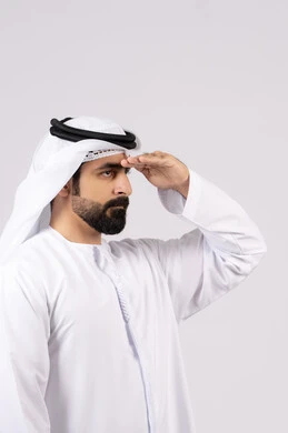 تعابير محاولة رؤية الأشياء البعيدة, مفهوم التطلع للمستقبل, النظر لمكان ما, بورتريه لرجل عربي خليجي إماراتي يرتدي الكندورة الغترة البيضاء يرفع يده إلى رأسه بإيماءات البحث عن شيء محدد, خلفية بيضاء