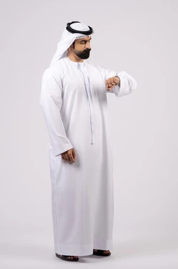 ايماءات اهميه الالتزام بالوقت وإنجاز المهامات والاعمال بدقه، مفهوم اهميه الوقت والالتزام بالمواعيد، بورتريه لرجل عربي خليجي اماراتي يرتدي الدكندورة والغترة ينظر الى ساعته الشخصيه ،  خلفيه بيضاء