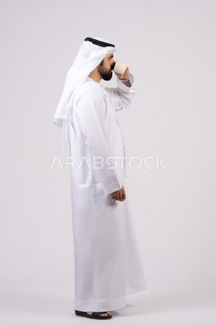 تأثير الكافيين على نشاط الدماغ والذاكرة، الاستمتاع بتناول المشروبات الساخنة والأعشاب الشتوية الدافئة، بورتريه لرجل عربي خليجي اماراتي يرتدي الكندورة والغترة يحمل فنجان من القهوة،صورة الجسم بالطول الكامل، خلفية بيضاء