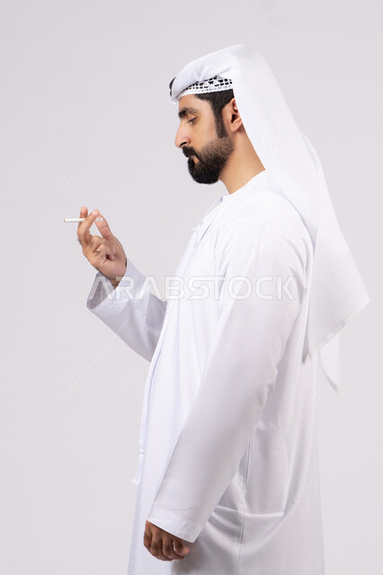 الادمان على التبغ و السجائر،عادات سلوكية ضارة، مفهوم مكافحة التدخين, تعاطي مواد سامة، بورتريه لرجل عربي اماراتي خليجي يرتدي الكندورة والغترة يقوم بتدخين السجائر، خلفيه بيضاء