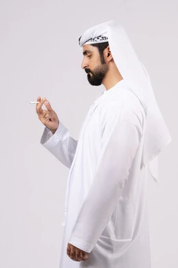 الادمان على التبغ و السجائر،عادات سلوكية ضارة، مفهوم مكافحة التدخين, تعاطي مواد سامة، بورتريه لرجل عربي اماراتي خليجي يرتدي الكندورة والغترة يقوم بتدخين السجائر، خلفيه بيضاء