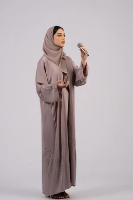 مواهب فنية موسيقية, بورتريه لفتاة عربية خليجية سعودية ترتدي العباءة والحجاب تقوم بعرض غنائي مسرحي, التفاعل والاندماج مع الموسيقى, الاستمتاع بممارسة هواية الغناء باستخدام الميكرفون,سيدة اماراتية تقوم بتقديم المواهب الصوتية بإيماءات الحماس والسرور, خلفية بيضاء