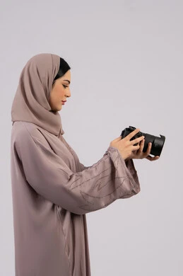 Using high-resolution digital cameras, using modern technical devices and technology, a portrait of an Emirati Gulf Arab woman wearing a hijab and abaya taking a souvenir photo with a camera, a Saudi photographer practicing the hobby of photography with expressions of pleasure, a female job and profession, professionalism in the art of photography, white background