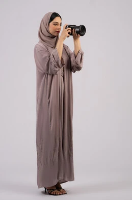 استخدام الأجهزة التقنية الحديثة والتكنولوجيا، بورتريه لإمراة عربية خليجية اماراتية ترتدي الحجاب والعباءة تقوم بالتقاط صورة تذكارية عبر كاميرا فوتوغرافية,  مصورة سعودية تمارس هواية التصوير بتعابير السرور،وظيفة ومهنة نسائية, احتراف فن التصوير الفوتوغرافي باستخدام كاميرات رقمية عالية الدقة, خلفية بيضاء