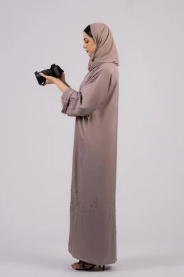 A Saudi photographer practices the hobby of photography with expressions of pleasure, a female job and profession, professionalism in the art of photography using high-resolution digital cameras, a side portrait of an Arab Gulf Emirati woman wearing a hijab and abaya taking a souvenir photo with a camera, white background