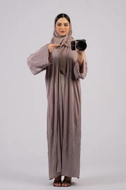 الاشارة الى الكاميرا ، احتراف فن التصوير الفوتوغرافي ، استخدام كاميرات رقمية عالية الدقة, استخدام الأجهزة التقنية الحديثة والتكنولوجيا، بورتريه لإمراة عربية خليجية اماراتية ترتدي الحجاب والعباءة تقوم بالتقاط صورة تذكارية عبر كاميرا فوتوغرافية,  مصورة سعودية تمارس هواية التصوير بتعابير السرور،وظيفة ومهنة نسائية,  خلفية بيضاء