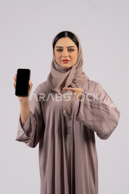 Emirati woman showing blank black screen, using modern technology and technology, having fun on mobile with friends, browsing social networking sites, portrait of a veiled Emirati Gulf Arab woman wearing an abaya using a mobile phone, full body, white background