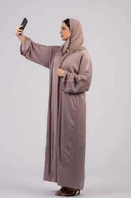 استخدام التكنولوجيا والتقنية الحديثة، قضاء وقت ممتع عبر الجوال مع الأصحاب، تصفح مواقع التواصل الاجتماعي، بورتريه لامرأة عربية خليجية اماراتية محجبة ترتدي العباءة تقوم بإستخدام الهاتف المحمول،سيدة اماراتية تلتقط السيلفي ، الجسم بالطول الكامل, خلفية بيضاء