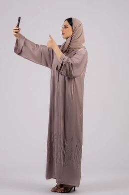 ايماءات الجودة والامتياز، التكنولوجيا والتقنية الحديثة، قضاء وقت ممتع عبر الجوال مع الأصحاب، تصفح مواقع التواصل الاجتماعي، بورتريه لامرأة عربية خليجية اماراتية محجبة ترتدي العباءة تقوم بإستخدام الهاتف المحمول،سيدة اماراتية تلتقط السيلفي ، الجسم بالطول الكامل, خلفية بيضاء