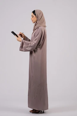 النظر بتعابير الاندماج , دمج التقنيات الحديثة والتكنولوجيا في الحياة العملية،بورتريه لإمرأة عربية خليجية سعودية محجبة ترتدي العباءة تقوم باستخدام قلم الجهاز اللوحي، سيدة اماراتية تقوم بتسجيل وتدوين البيانات والملاحظات، صورة للجسم بالكامل، خلفية بيضاء