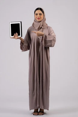 Gestures of interaction and integration, integration of modern technologies in practical life, portrait of a veiled Saudi Arabian Gulf woman wearing an abaya using a tablet, an Emirati woman displaying a blank black screen, a full body image, a white background