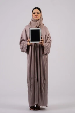 بورتريه لإمرأة عربية خليجية سعودية محجبة ترتدي العباءة تقوم باستخدام الجهاز اللوحي ،سيدة اماراتية تعرض شاشة سوداء فارغة، ايماءات التفاعل والاندماج , دمج التقنيات الحديثة في الحياة العملية، صورة للجسم بالكامل، خلفية بيضاء
