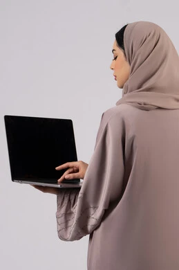 Working to achieve goals and strategies, a Saudi woman using a laptop to complete tasks, greeting people via video calls, managing and organizing business affairs, browsing the internet and using modern technology devices, an Arab Gulf Emirati girl working on a laptop, white background