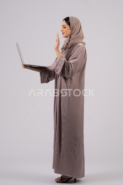 Saudi woman using laptop to complete tasks, greeting via video calls, managing and organizing business affairs, browsing the internet and using modern technology devices, Arab Gulf Emirati girl working on laptop, working to achieve goals and strategies, white background