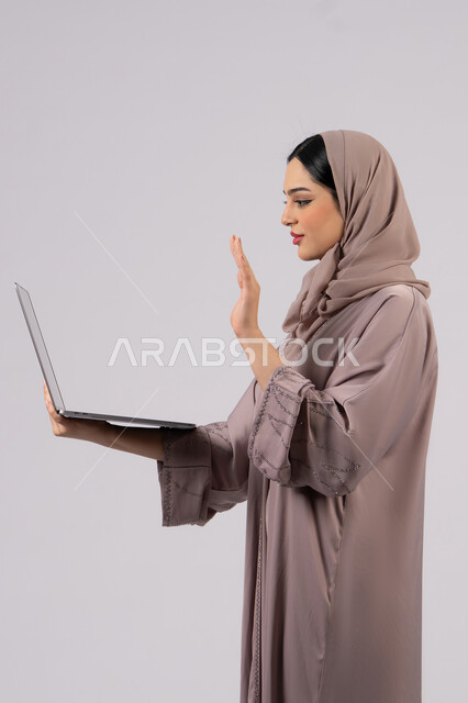 القاء التحية عبر مكالمات الفيديو، إدارة شؤون الأعمال وتنظيمها، تصفح الإنترنت وإستخدام اجهزة تقنية حديثة،فتاة عربية خليجية اماراتية تقوم بالعمل على الحاسوب المحمول، العمل لتحقيق الاهداف والاستراتيجيات، سيده سعودية تستخدم الحاسوب المحمول لإنجاز المهام،خلفية لكامل الجسم, خلفية بيضاء