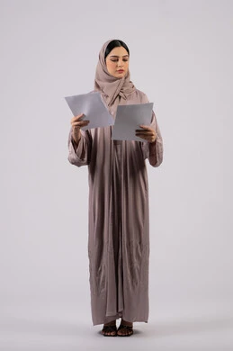 Reading notes and information, following up on plans and projects, work papers, writing down daily tasks, portrait of a veiled Arab Gulf Emirati woman wearing a black abaya holding a white paper in her hands, a young Saudi woman doing scientific research, white background