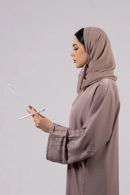 Daily task journaling, work papers, portrait of a veiled Emirati Gulf Arab woman wearing a black abaya holding a white paper and pen, a young Saudi woman doing scientific research, reading notes and information, following up on plans and projects, white background
