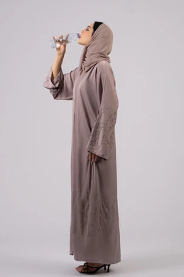 المداومة على شرب المياه ، المحافظة على سلامة الجهاز المناعي للجسم ,بورترية لامراة عربية خليجية امارتية محجبة ترتدي العباءة تقوم بالشرب من زجاجة ماء بلاستيكية صغيرة, سيدة سعودية تشعر بالعطش والجفاف , خلفية بيضاء