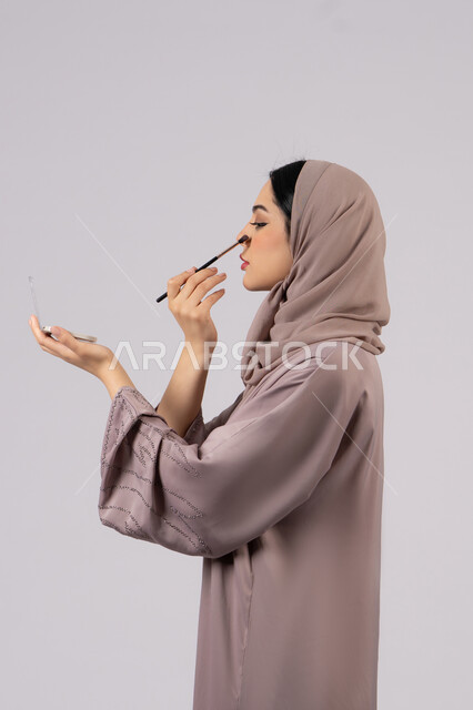 سيدة اماراتية تستخدم أدوات تجميل نسائيه عصريه، مكياج وميكاب تتوريال، التسويق لمنتجات التجميل ، بورتريه لفتاه عربيه سعودية خليجيه ترتدي العباءة والحجاب تحمل بيدها فرشاة توريد الخدود ، صالون نسائي راقي،مفهوم الانوثه والاهتمام بالمظهر الخارجي