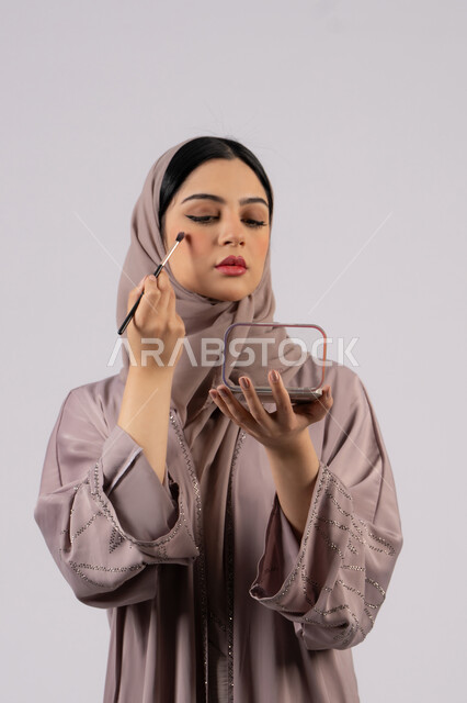 صالون نسائي راقي،مفهوم الانوثه والاهتمام بالمظهر الخارجي، سيدة اماراتية تستخدم أدوات تجميل نسائيه عصريه، مكياج وميكاب تتوريال، التسويق لمنتجات التجميل ،بورتريه لفتاه عربيه سعودية خليجيه ترتدي العباءة والحجاب تحمل بيدها فرشاة توريد الخدود