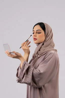 مفهوم الانوثه والاهتمام بالمظهر الخارجي، سيدة اماراتية تستخدم أدوات تجميل نسائيه عصريه، مكياج وميكاب تتوريال، صالون نسائي راقي، التسويق لمنتجات التجميل ،بورتريه لفتاه عربيه سعودية خليجيه ترتدي العباءة والحجاب تحمل بيدها فرشاة توريد الخدود