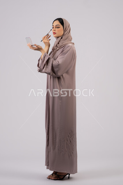 Emirati woman using modern women's cosmetics, the concept of femininity and interest in external appearance, makeup and makeup tutorial, high-end women's salon, marketing for beauty products, a side portrait of a Saudi Arabian Gulf girl wearing an abaya and hijab holding a blush brush in her hand