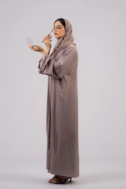 سيدة اماراتية تستخدم أدوات تجميل نسائيه عصريه، مفهوم الانوثه والاهتمام بالمظهر الخارجي، مكياج وميكاب تتوريال، صالون نسائي راقي، التسويق لمنتجات التجميل ،بورتريه من الجانب لفتاه عربيه سعودية خليجيه ترتدي العباءة والحجاب تحمل بيدها فرشاة توريد الخدود