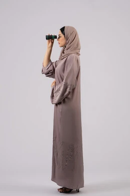 بورتريه من الجانب لامرأة عربية خليجية اماراتية محجبة ترتدي العباءة والحجاب تنظر من خلال منظار ،الرؤية بالعدسة المكبرة، حب الاستكشاف والمغامرة، ايماءات الدهشه و الاستغراب, التخطيط المستقبلي للأهداف و الطموحات، شابة سعودية تقوم برؤية الاشياء البعيدة عبر التلسكوب