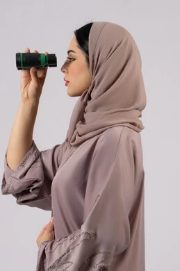 الرؤية بالعدسة المكبرة، حب الاستكشاف والمغامرة، ايماءات الدهشه و الاستغراب, التخطيط المستقبلي للأهداف و الطموحات، شابة سعودية تقوم برؤية الاشياء البعيدة عبر التلسكوب، بورتريه من الجانب لامرأة عربية خليجية اماراتية محجبة ترتدي العباءة والحجاب تنظر من خلال منظار